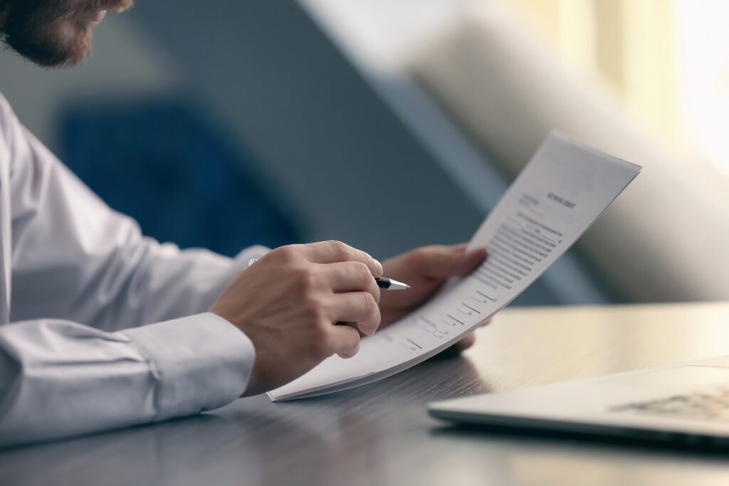 A man is writing case briefs on a piece of paper in front of a laptop.