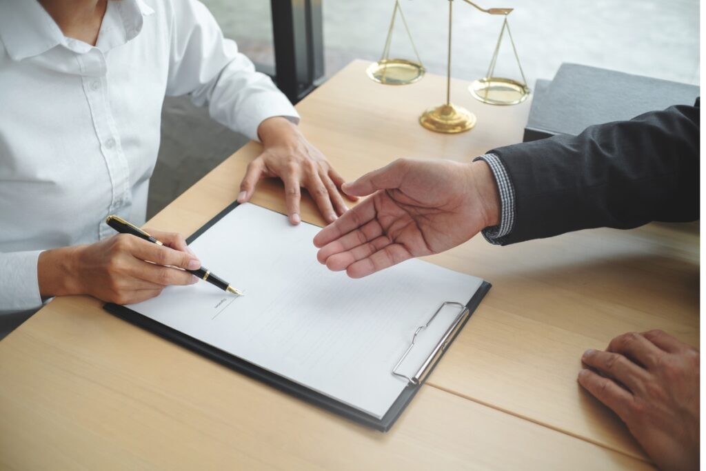 A lawyer shaking hands with a businessman over case briefs at a desk.