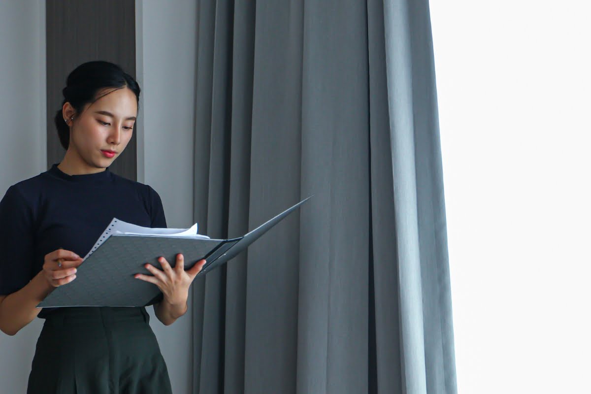 Asian woman engrossed in a book in front of a window.