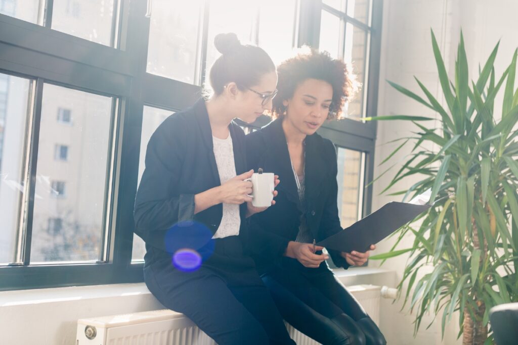 Two business women sitting on a window sill reviewing legal complaints.