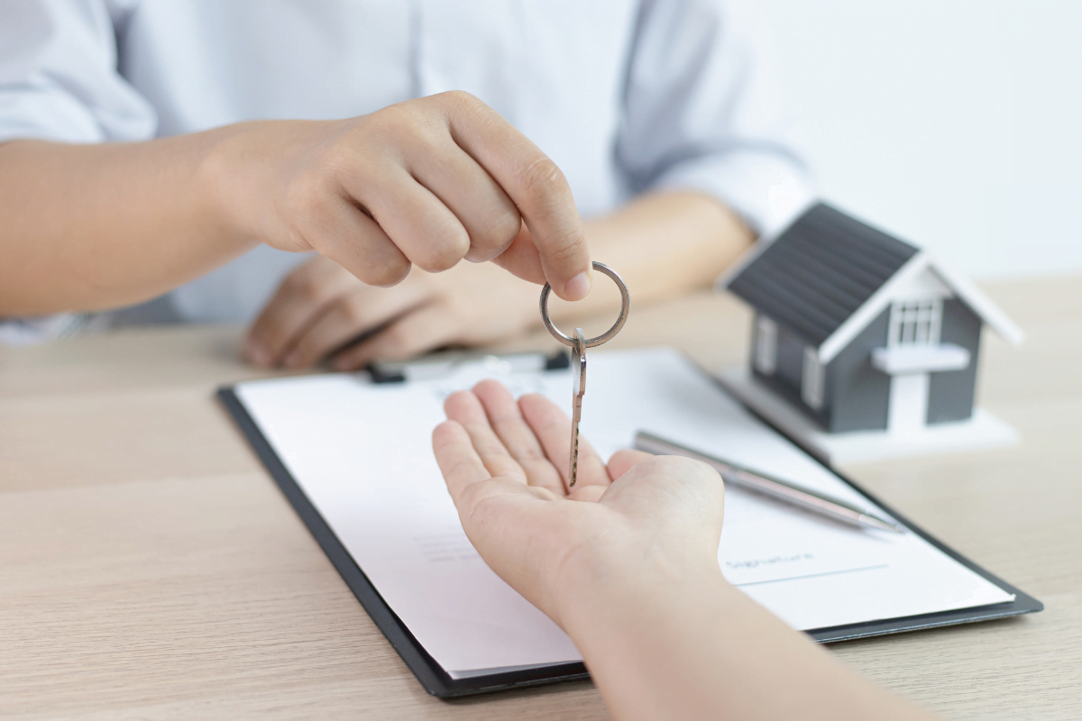 A hand is holding a house key on a desk, handing it to someone.