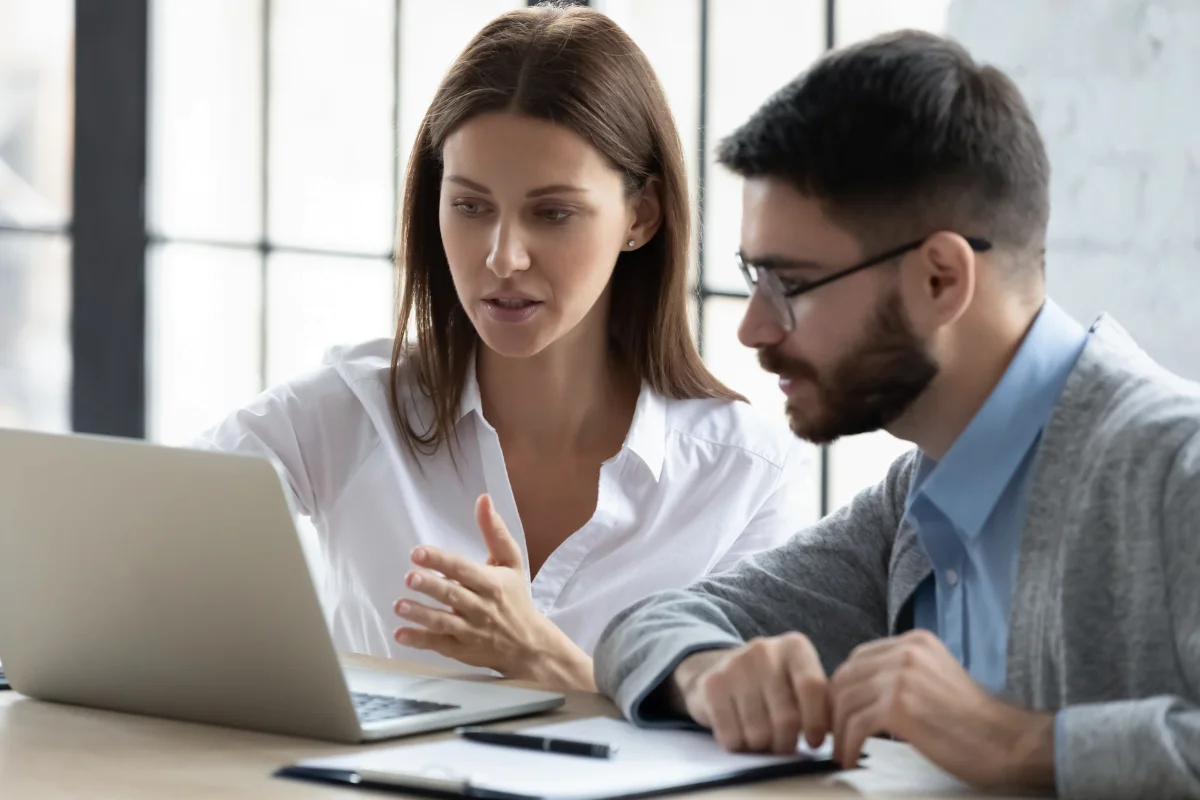 Two employers sitting at a table looking at a laptop and conducting screening for potential new hires.