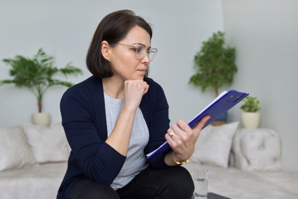 A woman is sitting on a couch, engaged in FCRA compliance measures, and looking at a clipboard.